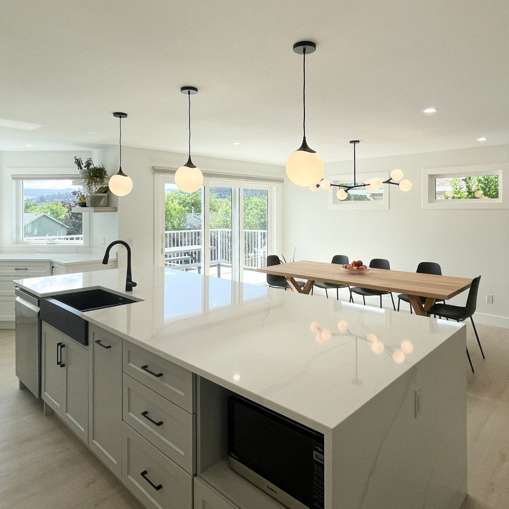 Open concept kitchen - large transitional galley light wood floor open concept kitchen idea with a farmhouse sink, shaker cabinets, white cabinets, quartz countertops, white backsplash, quartz backsplash, stainless steel appliances, an island and white countertops