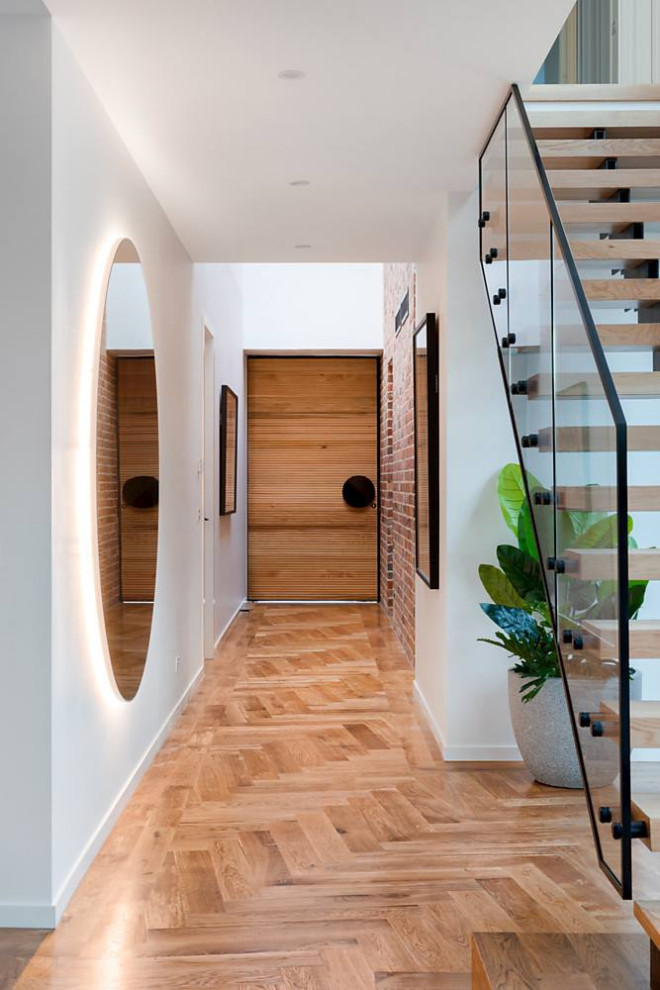 This is an example of a contemporary entryway in Melbourne with white walls, medium hardwood floors, a single front door, a medium wood front door and brown floor.