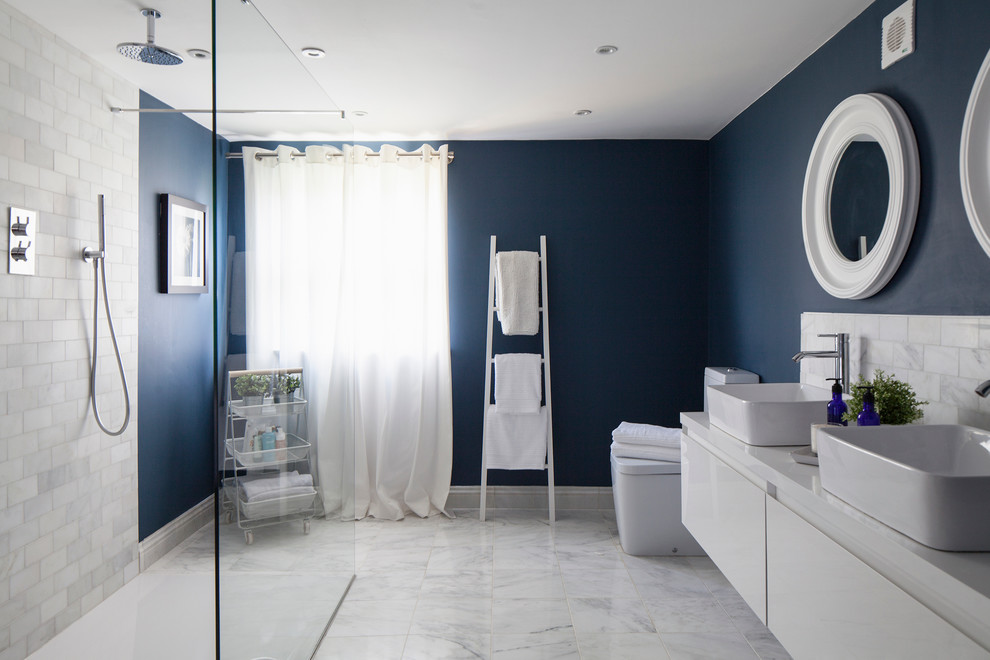 Design ideas for a mid-sized contemporary master bathroom in Surrey with flat-panel cabinets, white cabinets, an open shower, a one-piece toilet, white tile, stone tile, blue walls, marble floors, a vessel sink and an open shower.
