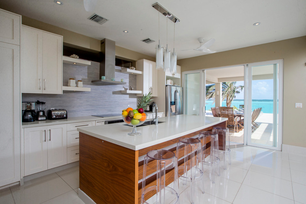 Photo of a mid-sized beach style single-wall eat-in kitchen in Other with recessed-panel cabinets, white cabinets, grey splashback, stainless steel appliances, porcelain floors, with island and white floor.