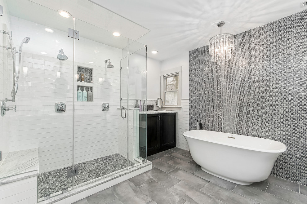 Inspiration for a transitional master bathroom in Columbus with recessed-panel cabinets, black cabinets, a freestanding tub, a double shower, black and white tile, gray tile, white walls, grey floor, a hinged shower door, mosaic tile, porcelain floors, a niche and a shower seat.