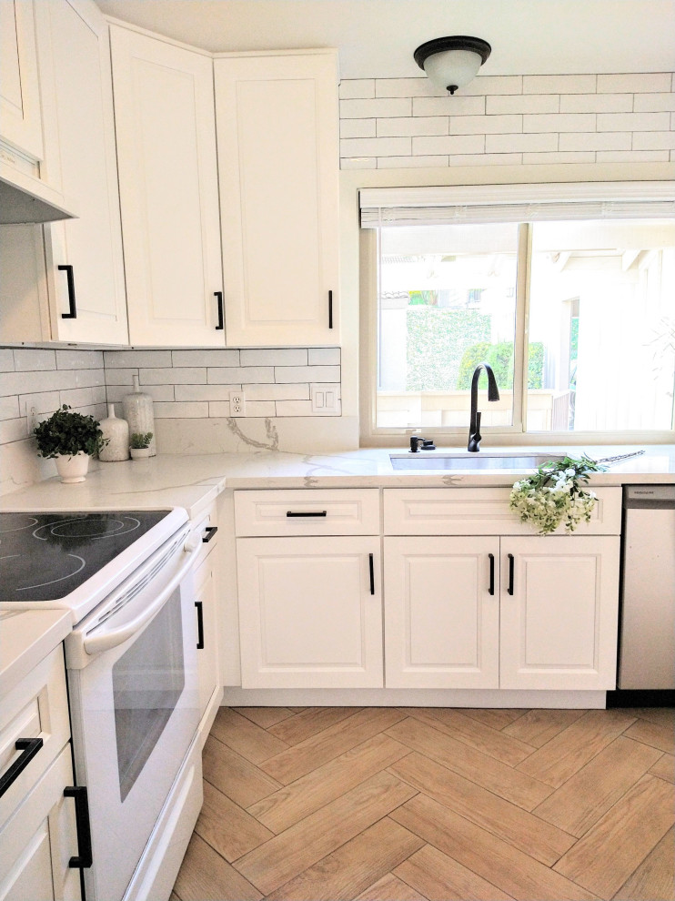 This is an example of a small farmhouse l-shaped kitchen pantry in San Diego with a single-bowl sink, raised-panel cabinets, white cabinets, engineered stone countertops, white splashback, ceramic splashback, white appliances, ceramic flooring, no island, brown floors and white worktops.