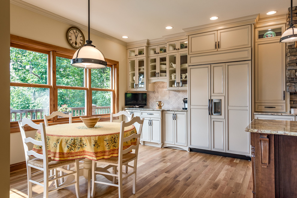Design ideas for a large traditional galley eat-in kitchen in Charlotte with an undermount sink, glass-front cabinets, beige cabinets, granite benchtops, beige splashback, stone tile splashback, panelled appliances, medium hardwood floors and with island.