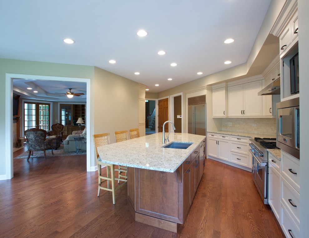 Open concept kitchen - mid-sized traditional l-shaped open concept kitchen idea in Chicago with a double-bowl sink, white cabinets, granite countertops, beige backsplash, stainless steel appliances, an island and recessed-panel cabinets