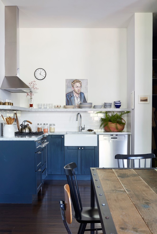 Industrial l-shaped eat-in kitchen in New York with a farmhouse sink, shaker cabinets, blue cabinets, white splashback, subway tile splashback, stainless steel appliances, dark hardwood floors, no island, brown floor and grey benchtop.