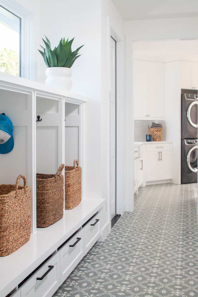 This is an example of a large beach style galley utility room in Orange County with shaker cabinets, white cabinets, quartz benchtops, white walls, concrete floors, a stacked washer and dryer, blue floor and white benchtop.