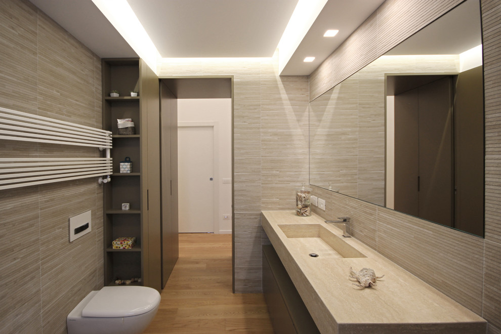 This is an example of a mid-sized modern 3/4 bathroom in Milan with flat-panel cabinets, light wood cabinets, a curbless shower, a wall-mount toilet, beige tile, porcelain tile, beige walls, medium hardwood floors, an integrated sink, marble benchtops, beige floor, an open shower and pink benchtops.