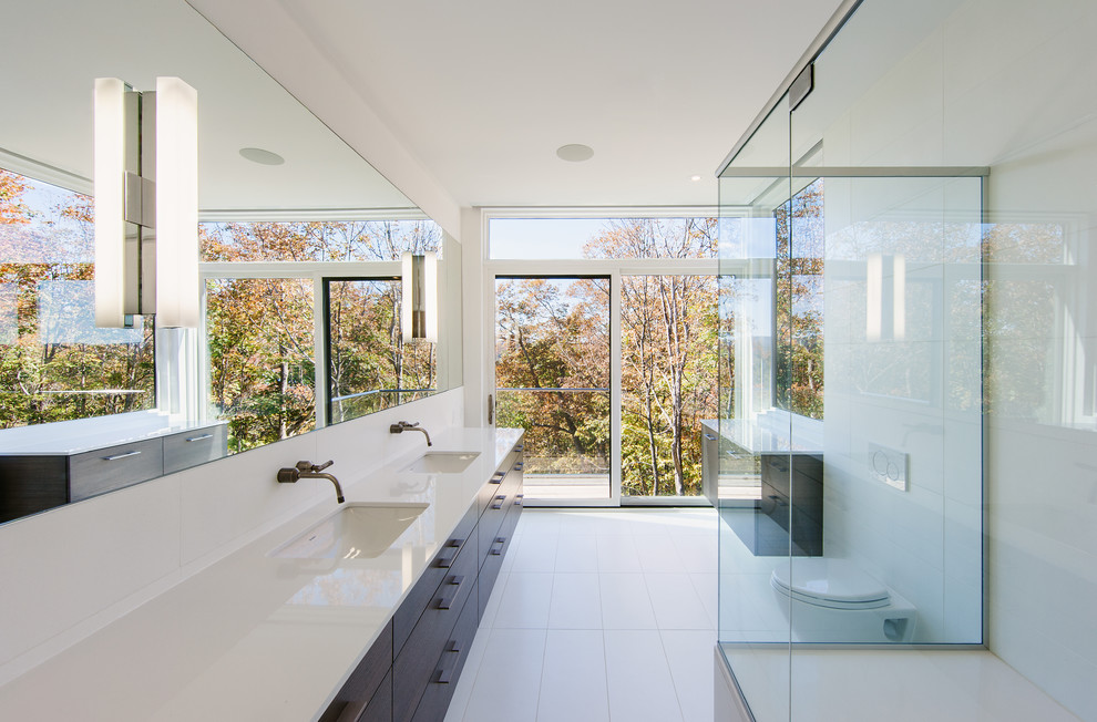 Inspiration for a contemporary bathroom in Montreal with flat-panel cabinets, dark wood cabinets, a corner shower, a wall-mount toilet, white tile, white walls and an undermount sink.