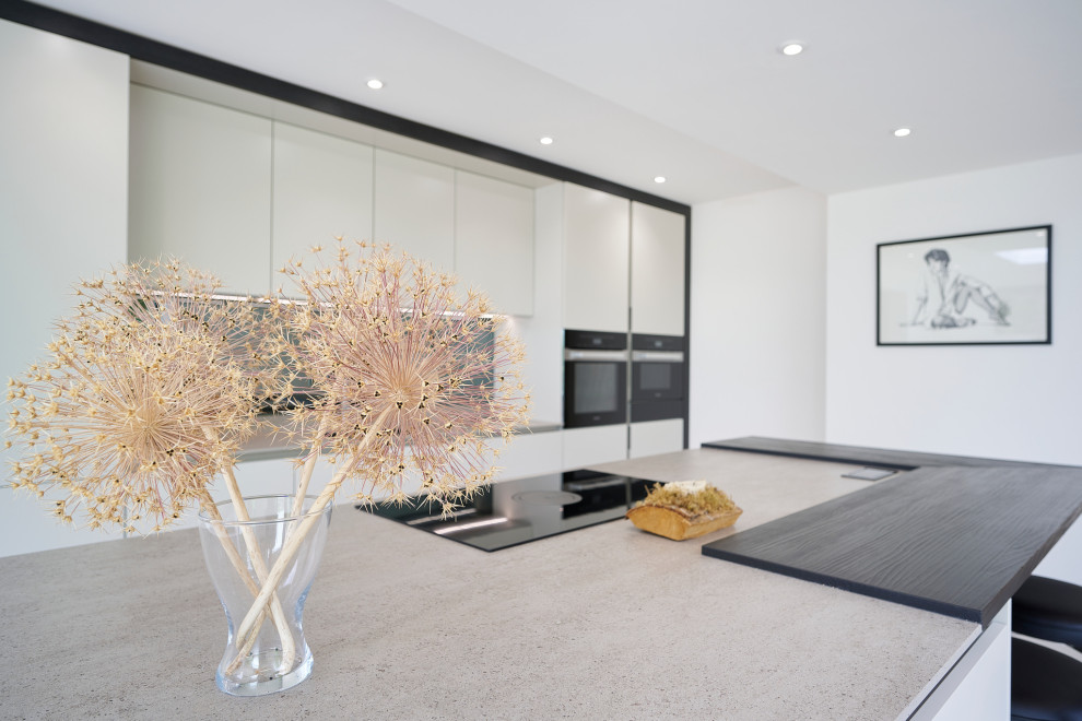 Expansive modern single-wall open plan kitchen in Sussex with an undermount sink, flat-panel cabinets, grey cabinets, quartz benchtops, mirror splashback, black appliances, ceramic floors, with island, grey floor, grey benchtop and recessed.