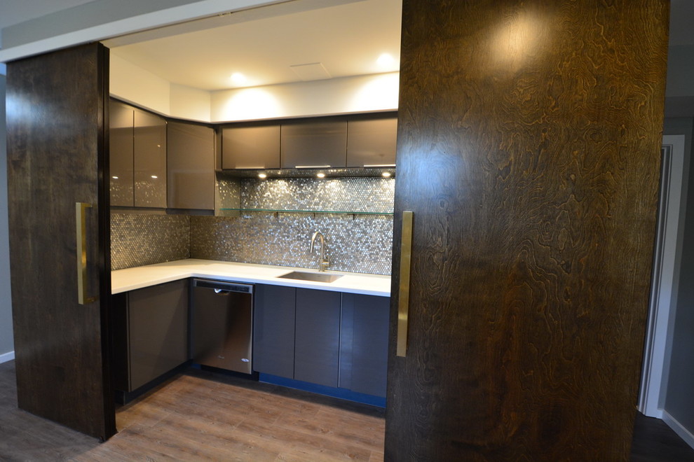 Photo of a large transitional u-shaped wet bar in Baltimore with dark hardwood floors, an undermount sink, flat-panel cabinets, grey cabinets, solid surface benchtops, grey splashback and mosaic tile splashback.
