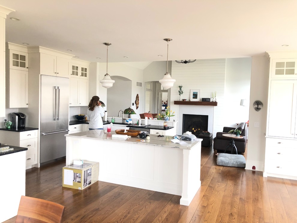 Photo of a large contemporary galley eat-in kitchen in Philadelphia with a drop-in sink, flat-panel cabinets, white cabinets, granite benchtops, grey splashback, ceramic splashback, stainless steel appliances, medium hardwood floors, with island, brown floor and multi-coloured benchtop.