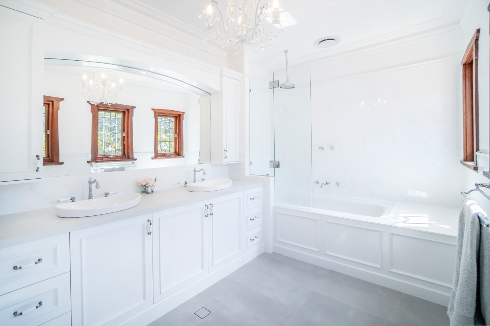 Idéer för att renovera ett vintage grå grått badrum, med luckor med profilerade fronter, vita skåp, ett undermonterat badkar, en dusch/badkar-kombination, vit kakel, keramikplattor, vita väggar, klinkergolv i keramik, ett fristående handfat, bänkskiva i kvarts, grått golv och med dusch som är öppen