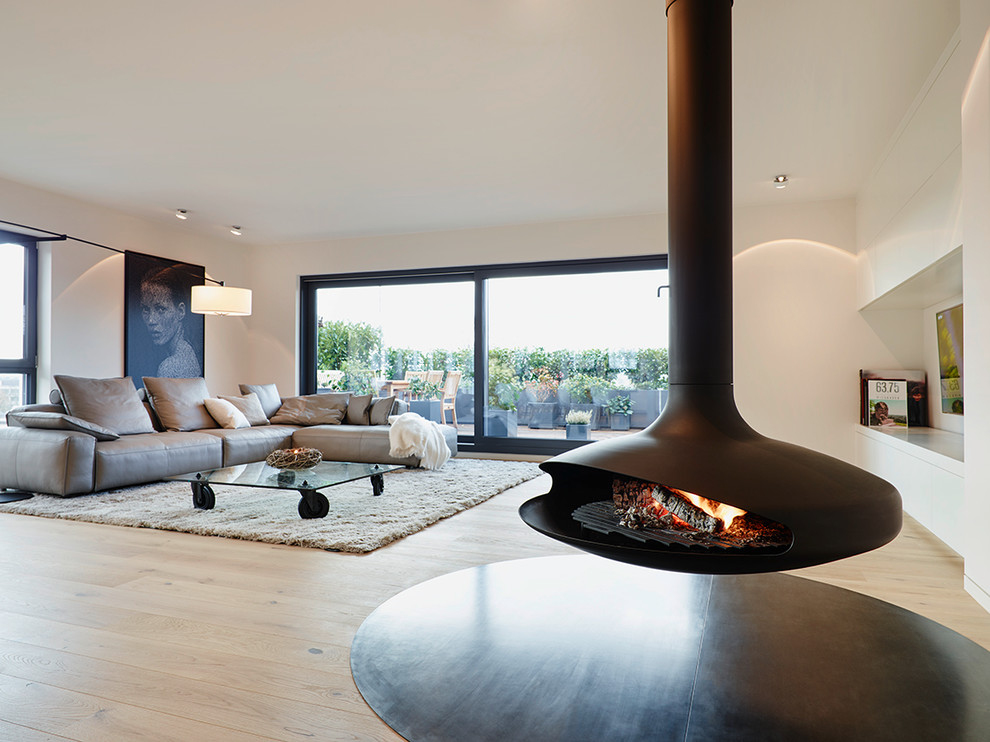 Photo of a large contemporary open concept living room in Frankfurt with white walls, light hardwood floors, a hanging fireplace and no tv.