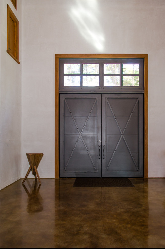 This is an example of a mediterranean front door in Houston with white walls, concrete floors, a double front door and a metal front door.