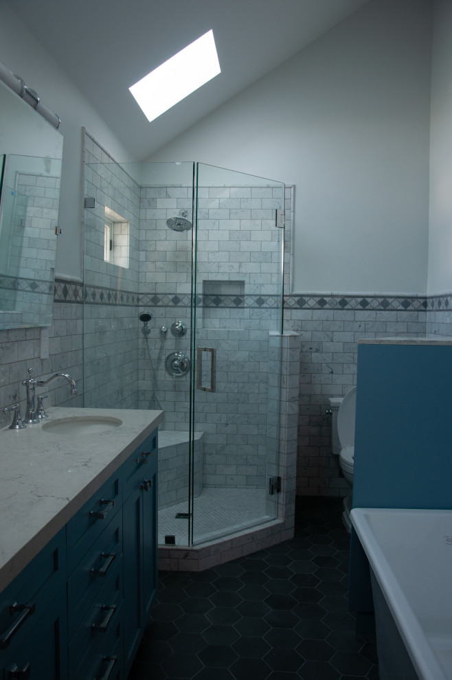 На фото: главная ванная комната среднего размера в классическом стиле с фасадами в стиле шейкер, синими фасадами, отдельно стоящей ванной, угловым душем, раздельным унитазом, серой плиткой, мраморной плиткой, серыми стенами, полом из керамогранита, врезной раковиной, столешницей из искусственного кварца, серым полом, душем с распашными дверями, белой столешницей, сиденьем для душа, тумбой под две раковины, встроенной тумбой, сводчатым потолком и панелями на стенах