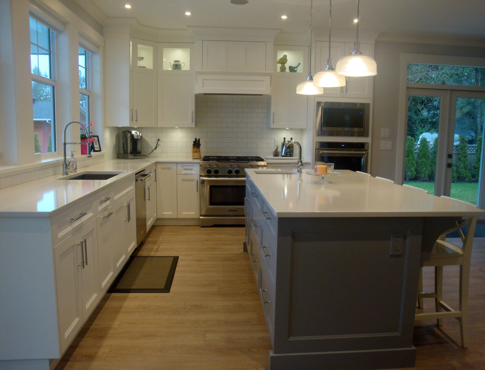 Transitional u-shaped eat-in kitchen in Vancouver with an undermount sink, recessed-panel cabinets, white cabinets, quartz benchtops, white splashback, ceramic splashback, stainless steel appliances and with island.