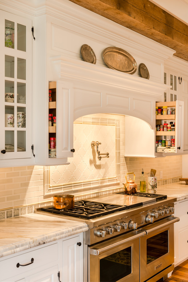 This is an example of an expansive country l-shaped eat-in kitchen in Philadelphia with a farmhouse sink, raised-panel cabinets, white cabinets, marble benchtops, white splashback, stone tile splashback, stainless steel appliances, medium hardwood floors, with island and brown floor.