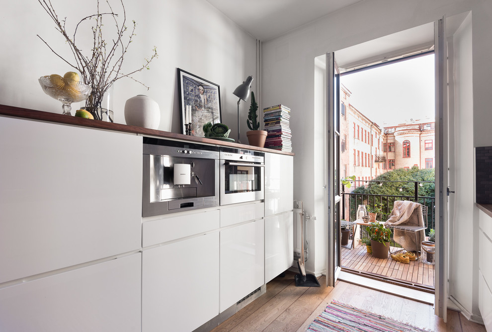 This is an example of a mid-sized scandinavian single-wall open plan kitchen in Gothenburg with flat-panel cabinets, white cabinets, wood benchtops, grey splashback, mosaic tile splashback, white appliances, medium hardwood floors, no island and brown floor.