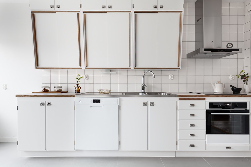 Photo of a midcentury eat-in kitchen in Malmo with a double-bowl sink, white cabinets, stainless steel benchtops, white splashback, white appliances, flat-panel cabinets and no island.
