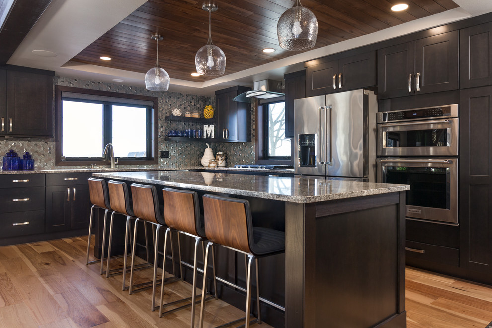 Kitchen - transitional l-shaped medium tone wood floor and brown floor kitchen idea with an undermount sink, shaker cabinets, black cabinets, gray backsplash, mosaic tile backsplash, stainless steel appliances, an island and gray countertops
