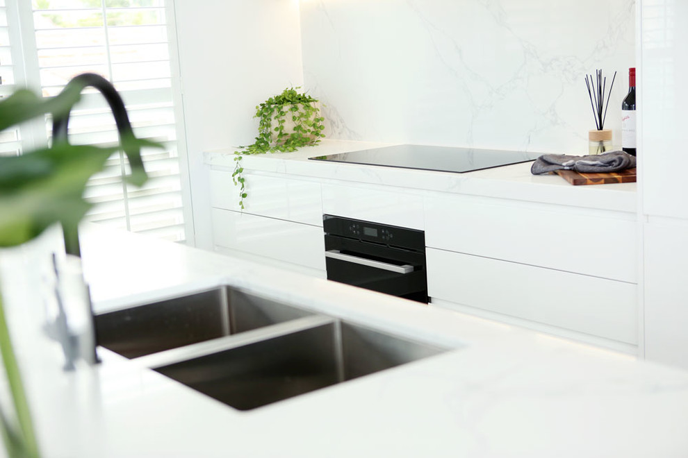 Photo of a modern open plan kitchen in Melbourne with a double-bowl sink, white cabinets, marble benchtops, white splashback, marble splashback, black appliances, with island and white benchtop.