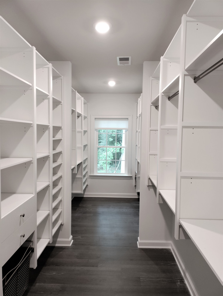 Diseño de armario vestidor grande con armarios con paneles lisos, puertas de armario blancas y suelo de madera oscura