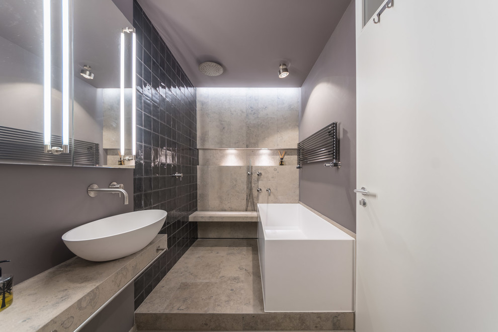 Photo of a small modern 3/4 bathroom in Munich with flat-panel cabinets, grey cabinets, a freestanding tub, an open shower, a wall-mount toilet, black tile, ceramic tile, grey walls, limestone floors, a vessel sink, limestone benchtops, grey floor and an open shower.