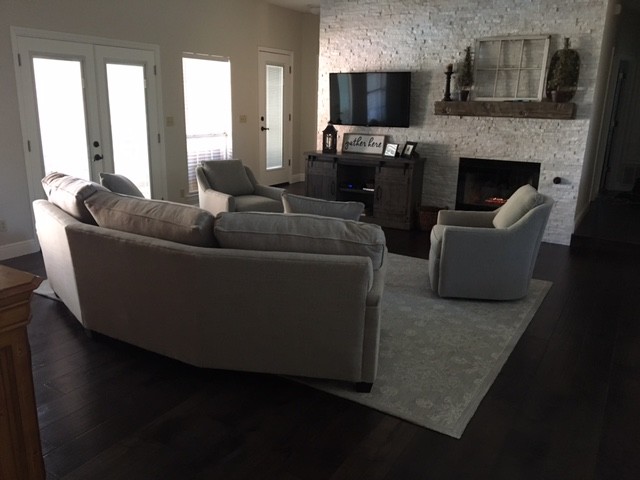 Inspiration for a large transitional open concept family room in Miami with a home bar, white walls, dark hardwood floors, a standard fireplace, a wall-mounted tv, brown floor and a stone fireplace surround.