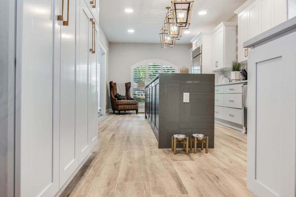 Large transitional l-shaped porcelain tile and gray floor kitchen pantry photo in Houston with a farmhouse sink, shaker cabinets, white cabinets, quartzite countertops, white backsplash, glass tile backsplash, stainless steel appliances, an island and white countertops
