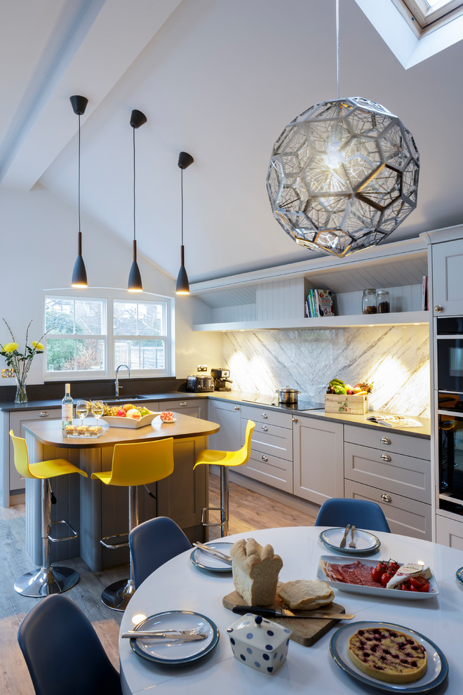 Photo of a traditional open plan kitchen in Berkshire with shaker cabinets, grey cabinets, quartzite benchtops, marble splashback, black appliances, with island, a double-bowl sink, white splashback, vinyl floors and brown floor.