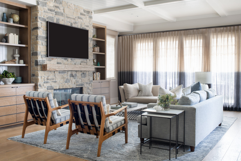 This is an example of a mid-sized beach style open concept living room in Los Angeles with beige walls, light hardwood floors, a standard fireplace, a stone fireplace surround, a wall-mounted tv, beige floor and coffered.