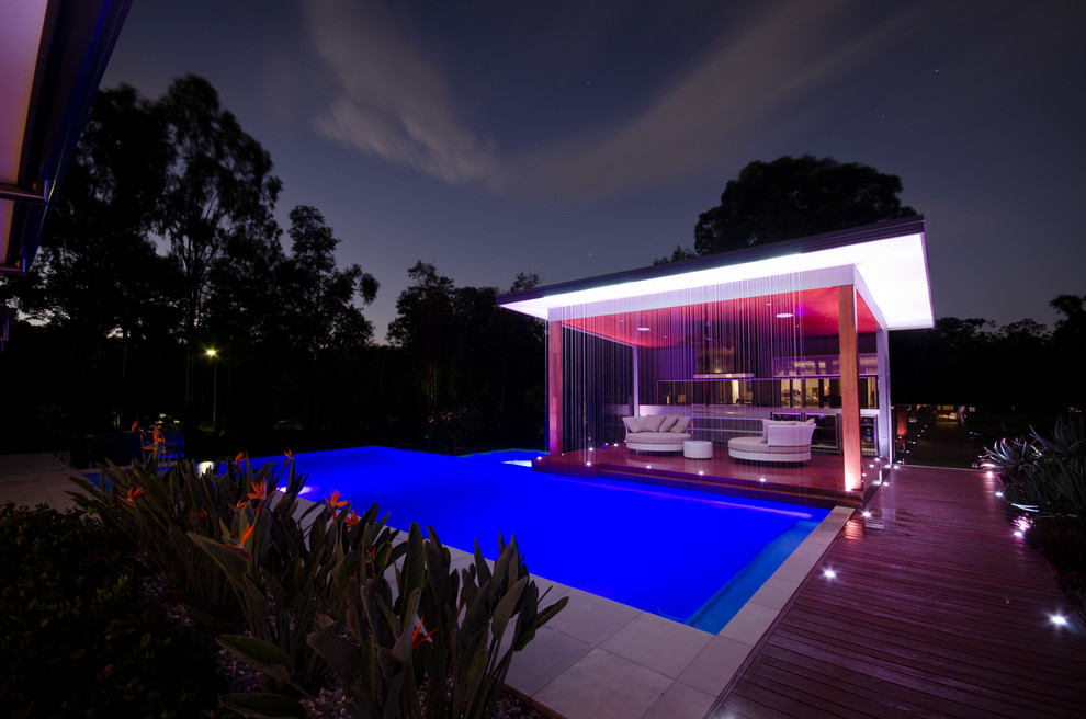This is an example of a large contemporary side yard custom-shaped infinity pool in Other with a hot tub and decking.