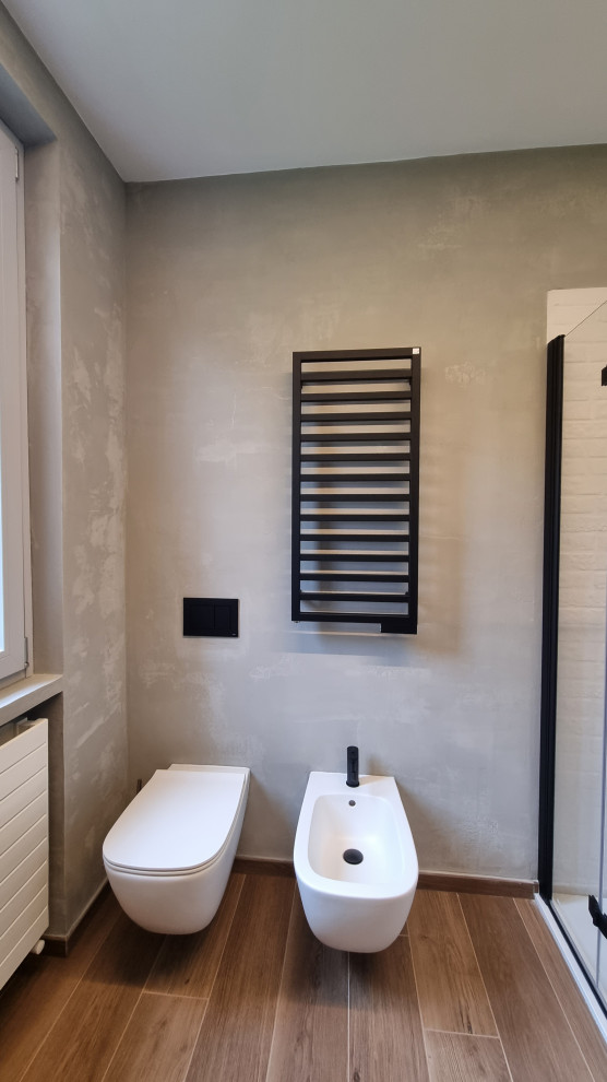 Small industrial powder room in Milan with flat-panel cabinets, grey cabinets, a wall-mount toilet, beige tile, beige walls, porcelain floors, a vessel sink, wood benchtops, brown floor, beige benchtops, a floating vanity, recessed and brick walls.