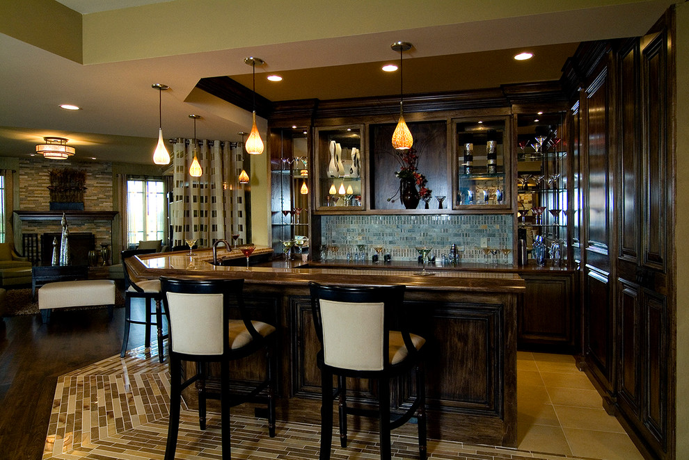 Photo of a mid-sized traditional l-shaped seated home bar in Chicago with raised-panel cabinets, dark wood cabinets, wood benchtops, blue splashback, ceramic splashback, ceramic floors, beige floor and brown benchtop.