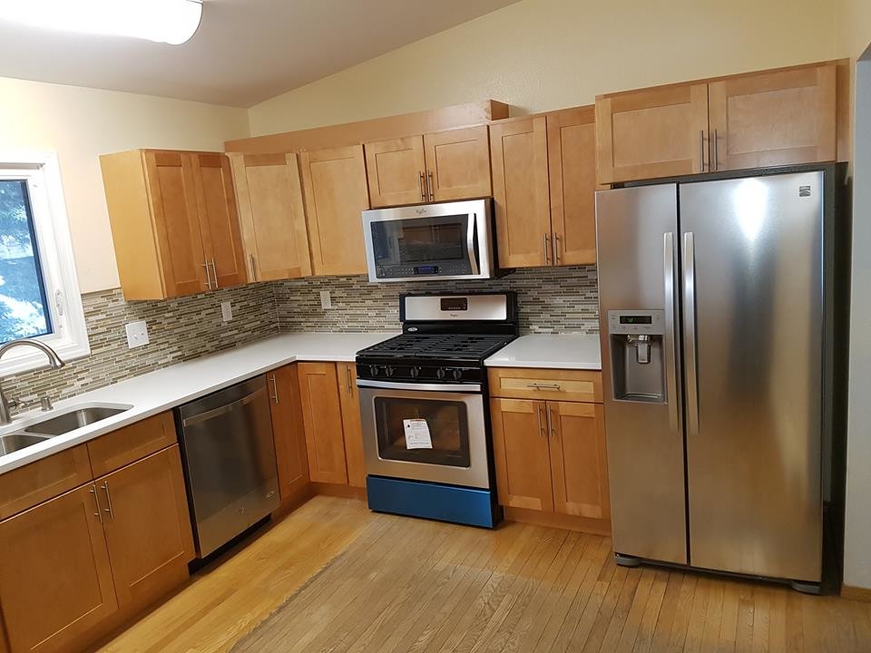 Inspiration for a mid-sized transitional light wood floor kitchen remodel with a double-bowl sink, shaker cabinets, light wood cabinets, solid surface countertops, multicolored backsplash and matchstick tile backsplash