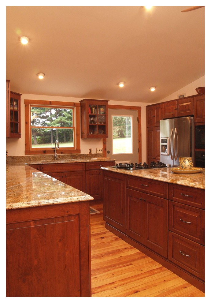 Photo of a mid-sized country u-shaped separate kitchen in Baltimore with raised-panel cabinets, medium wood cabinets, granite benchtops, grey splashback, stone slab splashback, light hardwood floors, with island, an undermount sink and black appliances.
