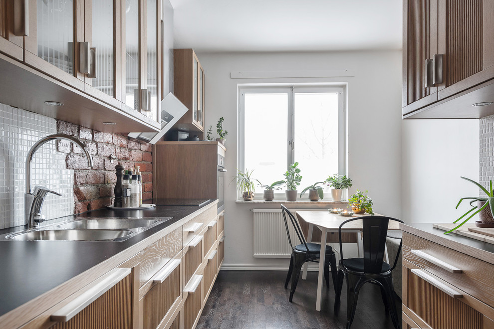 Design ideas for a scandinavian galley eat-in kitchen in Stockholm with no island, a double-bowl sink, glass-front cabinets, light wood cabinets, white splashback, dark hardwood floors and black benchtop.