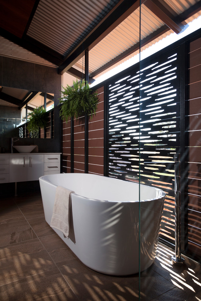 Inspiration for a large tropical master bathroom in Darwin with a wall-mount sink, raised-panel cabinets, white cabinets, limestone benchtops, a freestanding tub, a double shower, a one-piece toilet, brown tile, stone tile, black walls and ceramic floors.