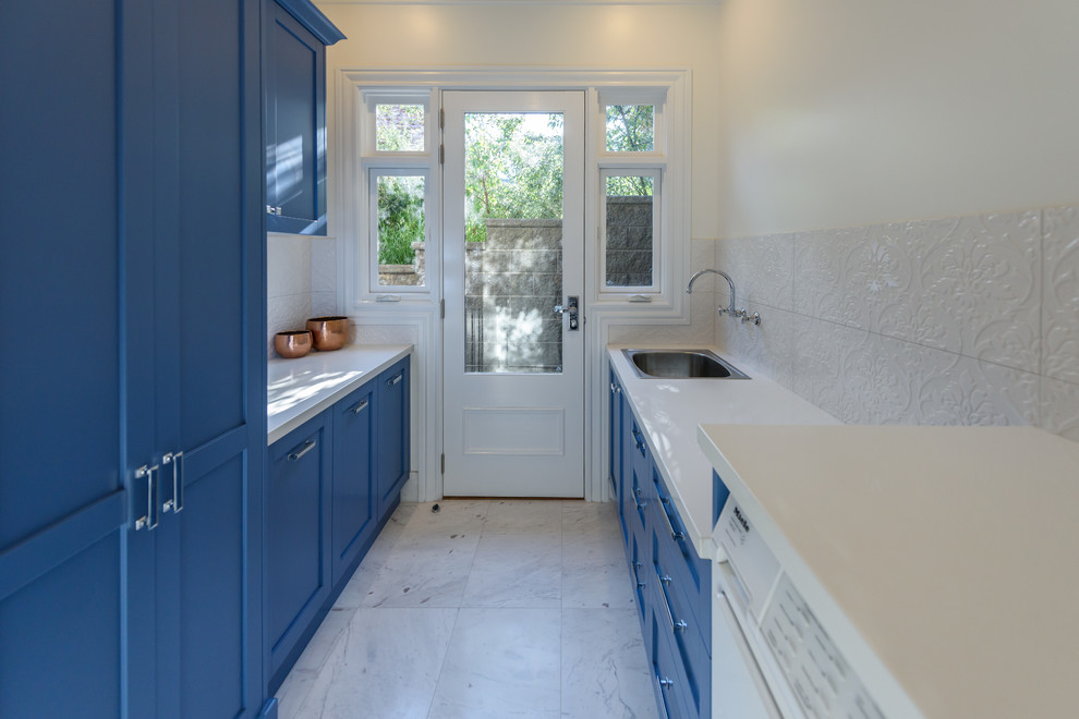 Design ideas for a mid-sized traditional galley dedicated laundry room in Melbourne with a single-bowl sink, recessed-panel cabinets, blue cabinets, quartz benchtops, white walls, marble floors and a side-by-side washer and dryer.