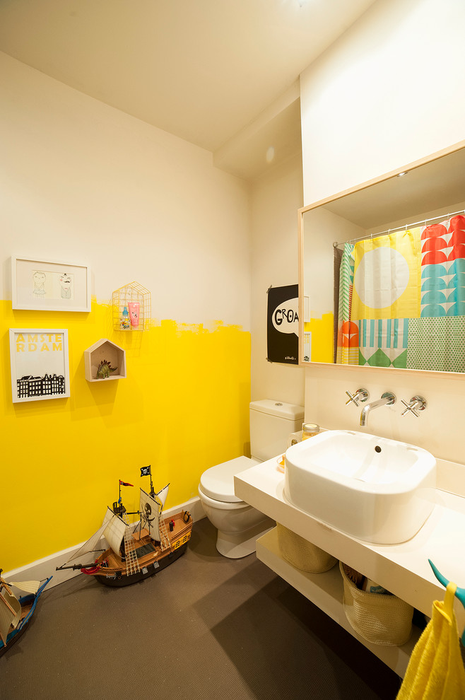 Photo of a small eclectic kids bathroom in Other with a vessel sink, a two-piece toilet, yellow walls, concrete floors and solid surface benchtops.