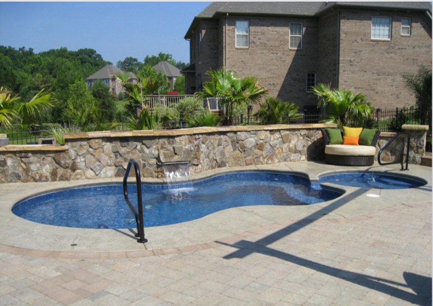 Design ideas for a mid-sized tropical backyard custom-shaped pool in Charlotte with a hot tub and brick pavers.