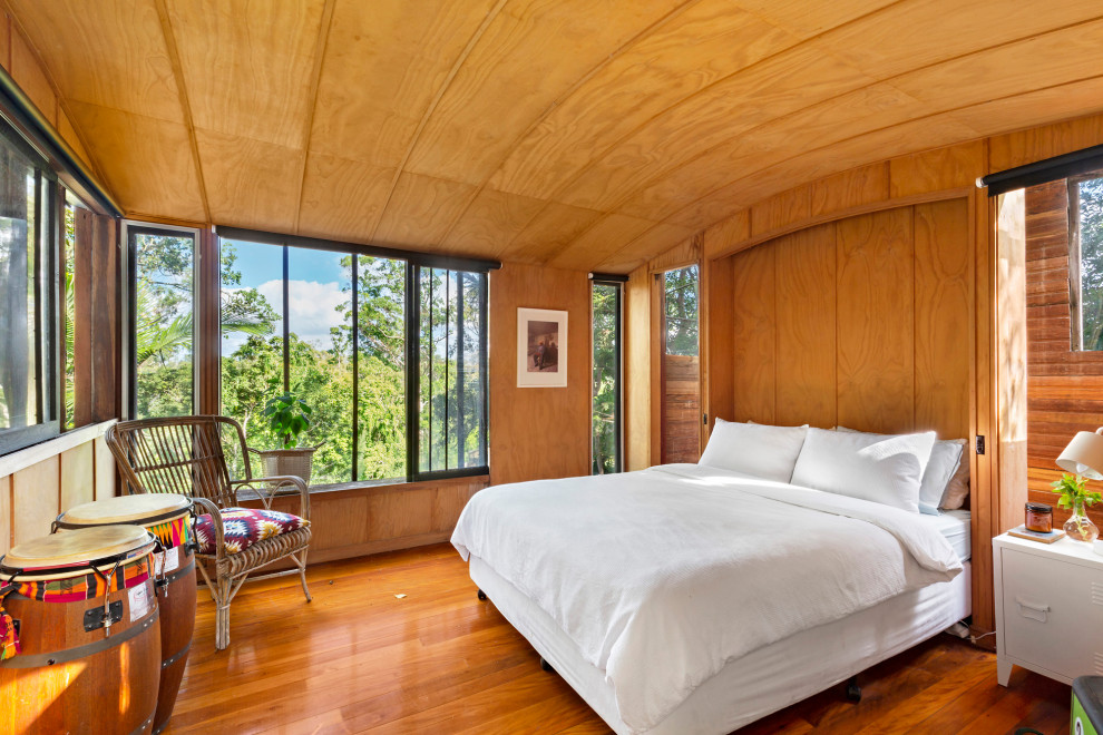 Expansive midcentury bedroom in Brisbane with brown walls, light hardwood floors, brown floor, vaulted and panelled walls.