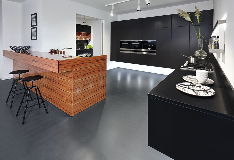 Photo of a large contemporary u-shaped open plan kitchen in Other with flat-panel cabinets, black cabinets, wood benchtops, stainless steel appliances, a peninsula, a drop-in sink, white splashback and linoleum floors.