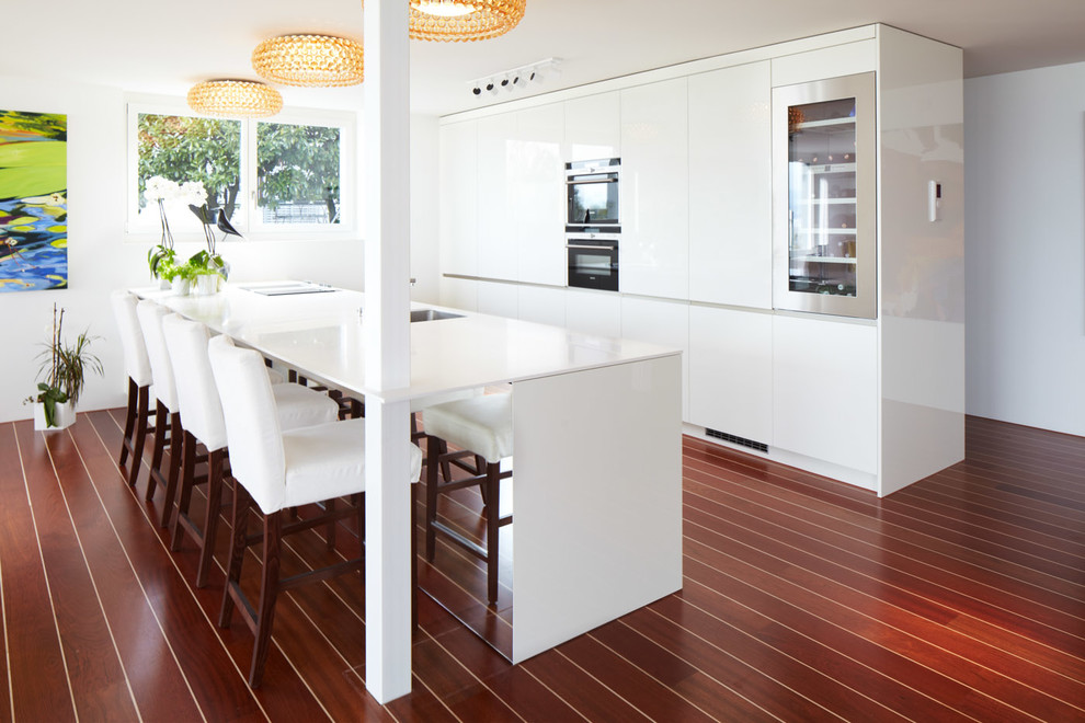 Large contemporary open plan kitchen in Hamburg with an undermount sink, flat-panel cabinets, white cabinets, panelled appliances, painted wood floors and with island.