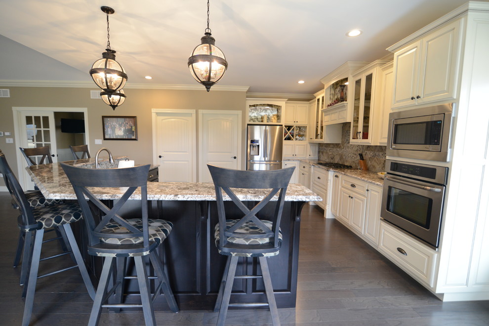 Huge transitional l-shaped medium tone wood floor eat-in kitchen photo in Chicago with a farmhouse sink, raised-panel cabinets, white cabinets, granite countertops, gray backsplash, glass tile backsplash, stainless steel appliances and an island