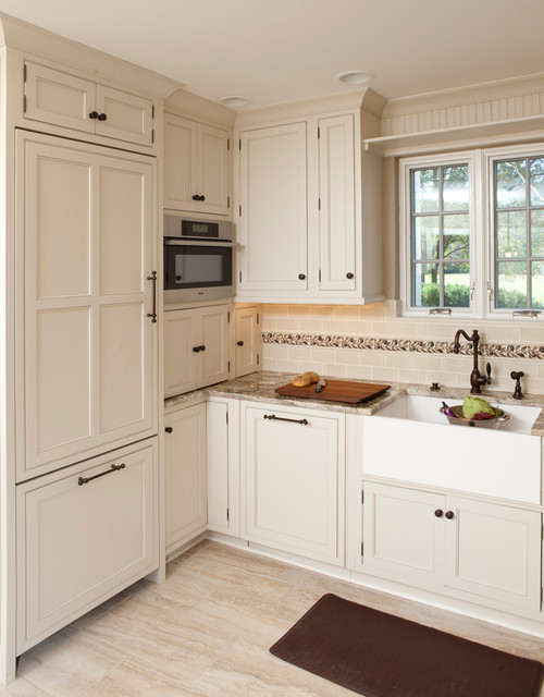 Compact cottage-style kitchen with cream inset RTA cabinets, panel-ready fridge, built-in microwave tower, farmhouse sink, granite counters, and a decorative backsplash border.