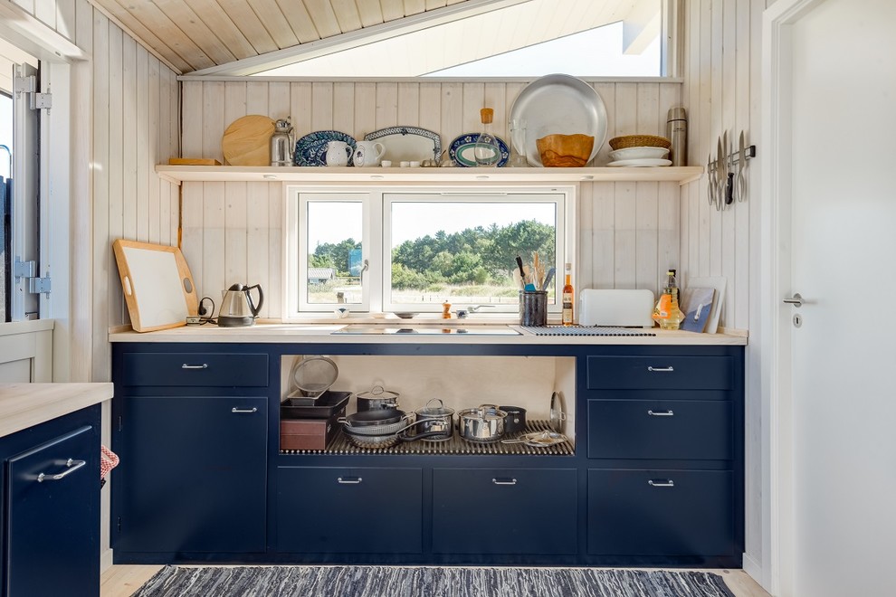 Photo of a small country kitchen in Copenhagen with flat-panel cabinets, blue cabinets, wood benchtops and light hardwood floors.