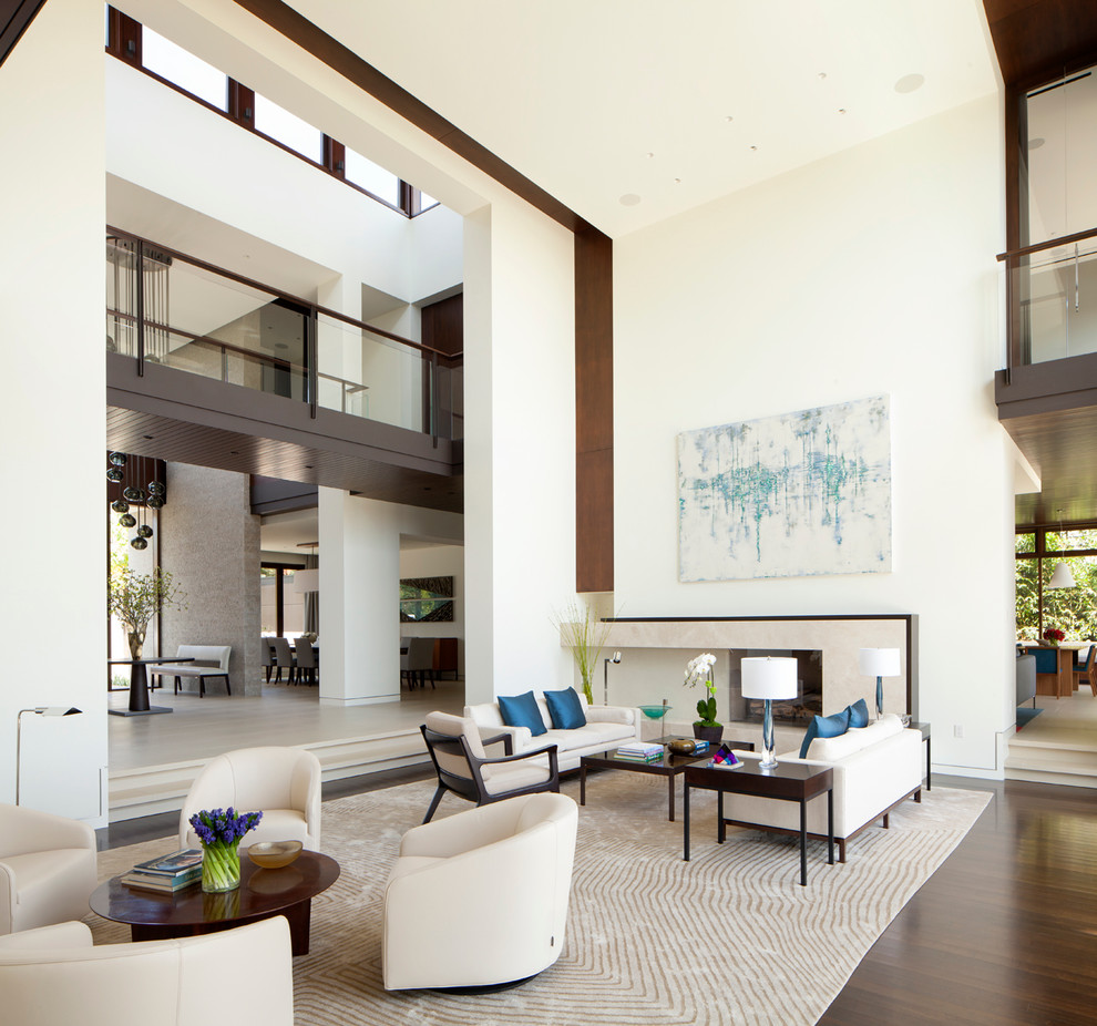 Expansive contemporary open concept living room in Los Angeles with white walls, dark hardwood floors, a standard fireplace, a stone fireplace surround and brown floor.