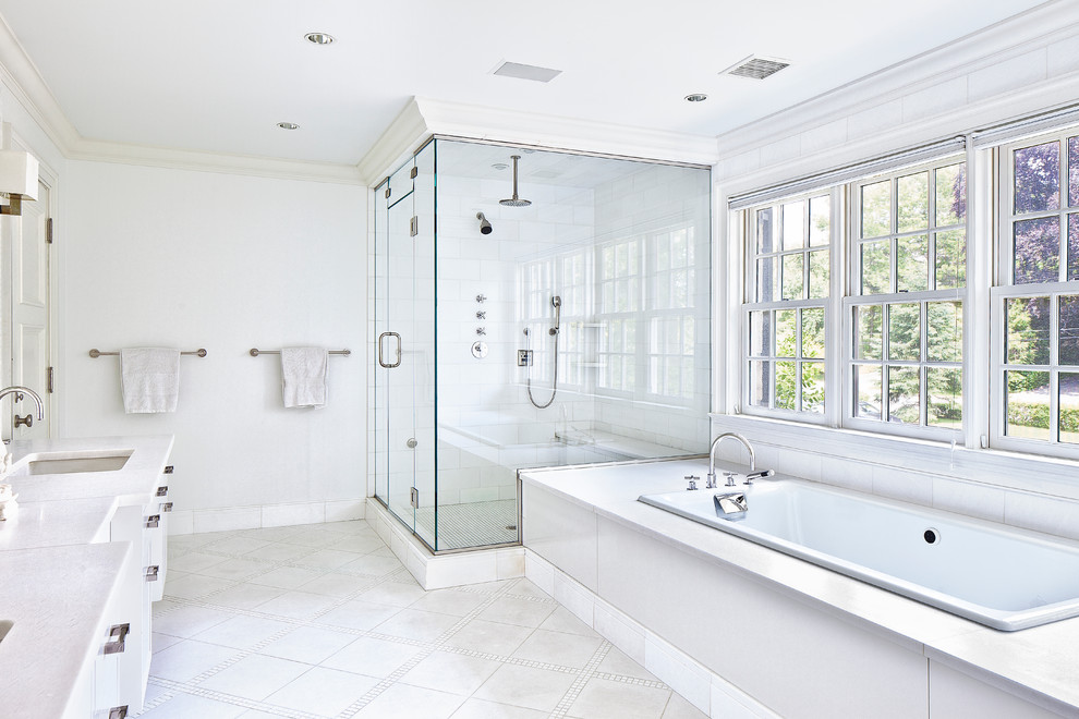 This is an example of a large transitional master bathroom in New York with white walls, shaker cabinets, white cabinets, a drop-in tub, an alcove shower, a two-piece toilet, white tile, porcelain tile, ceramic floors, an undermount sink, marble benchtops, white floor and a hinged shower door.
