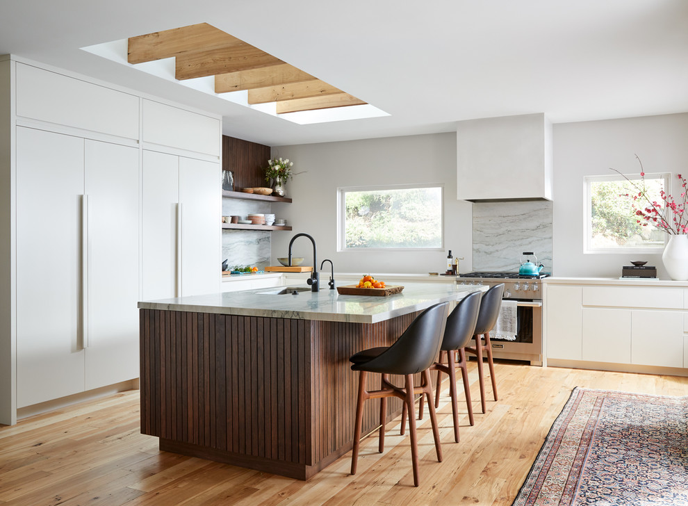 Design ideas for a scandinavian l-shaped kitchen in San Francisco with a single-bowl sink, flat-panel cabinets, white cabinets, stone slab splashback, light hardwood floors, with island, white benchtop, stainless steel appliances, grey splashback and beige floor.